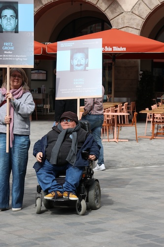Oswald Utz sitzt im Rollstuhl und hält eine Tafel des Opfers